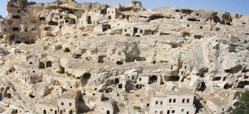 The abandoned cliff village of Cavusin, its cave dwellings carved into pale volcanic rock above the stone houses below