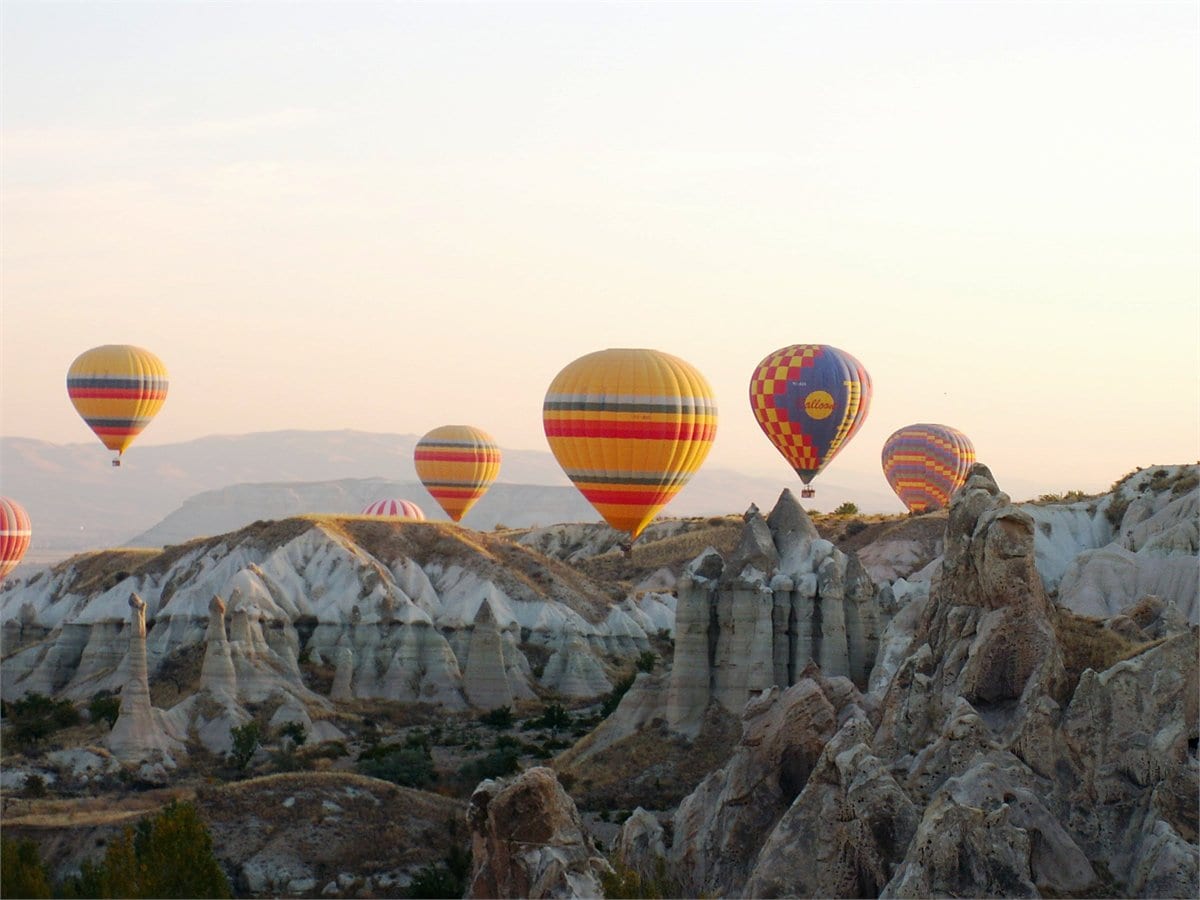 Hot air balloons lifting off into a calm dawn sky over Cappadocia