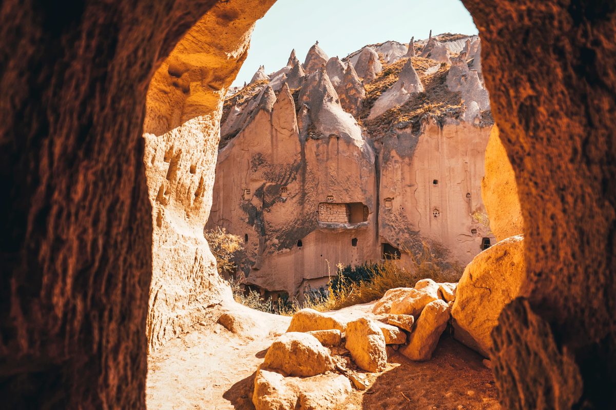 Cliffs pitted with carved windows and cave rooms at the Zelve Open Air Museum in Cappadocia, seen through the mouth of a rock-cut cave